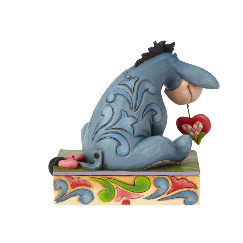 Eeyore figurine from Jim Shore's Disney Traditions, looking at a red and pink checkered heart, sitting on a decorated base.