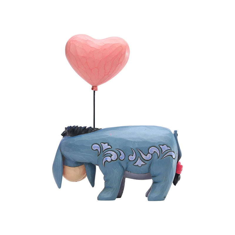 Side view of a Jim Shore Disney Traditions figurine showing Eeyore with a large, pink heart-shaped balloon attached to his back.