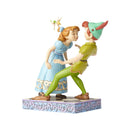 Figurine from Jim Shore's Disney Traditions, featuring Wendy leaning in for a kiss with Peter Pan, as Tinker Bell looks on, all set on a decorative base.