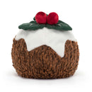 A plush toy designed as a Christmas pudding with a rich brown textured body, topped with white faux icing, two red berries, and a detailed green leaf.