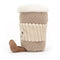 A plush toy resembling a coffee cup with a creamy top, beige ribbed body, a joyful face, and a brown corded leg.