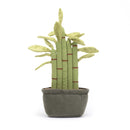 A plush bamboo plant with five green linen stems, red-brown stitches, suede-like leaves, sitting in a suede pot with fluffy soil. It has corded feet and a cheerful face.