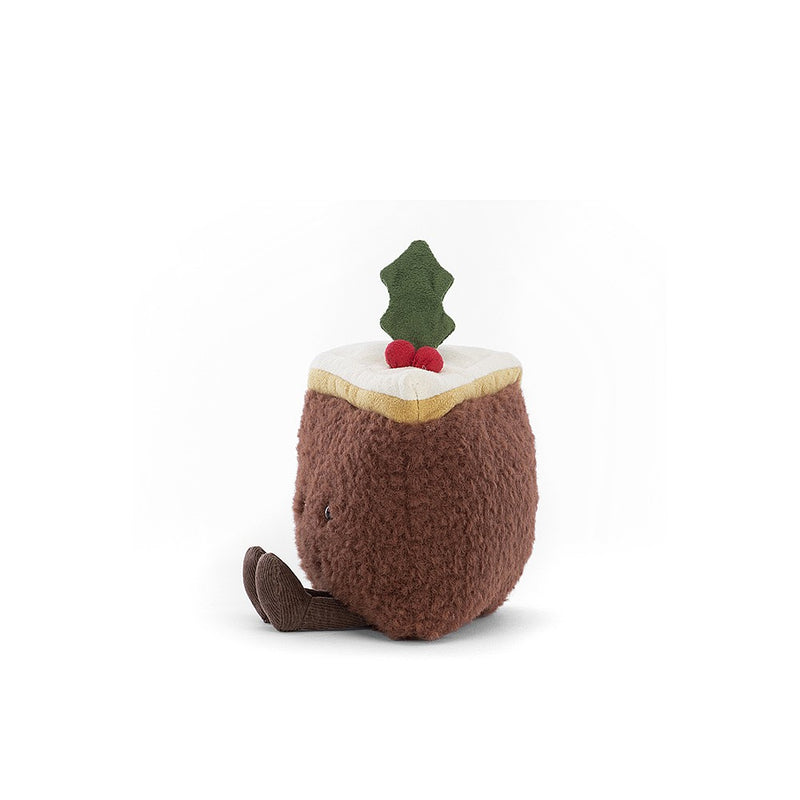 A plush toy resembling a festive slice of Christmas cake, complete with marzipan, icing, and a holly sprig accent. It has twinkling eyes, a stitched smile, and raisin-like boots.