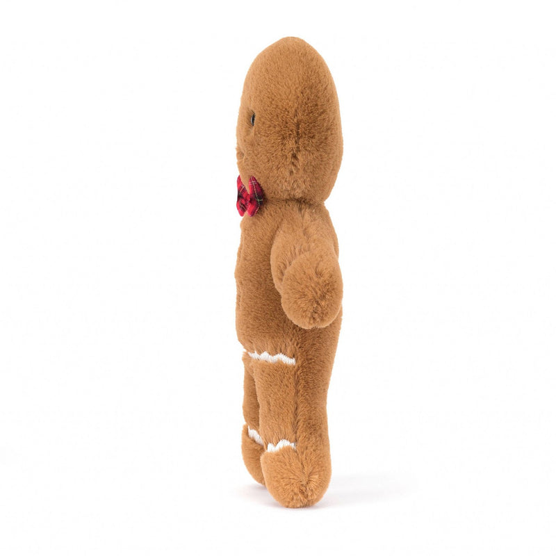 A side view of a plush gingerbread man toy, showcasing its brown fur, white icing details on the legs and arms, and a red tartan bow tie on the back.