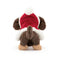 A rear view of a brown plush toy dog wearing a festive red cloak with white trim, showcasing its fluffy tail and hind legs.