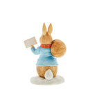 Photo from the back: Peter Rabbit in his winter attire, carrying a bag of delightful surprises and holding a sign that reads "With Love"