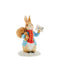Peter Rabbit in his winter attire, carrying a bag of delightful surprises and holding a sign that reads "With Love,"